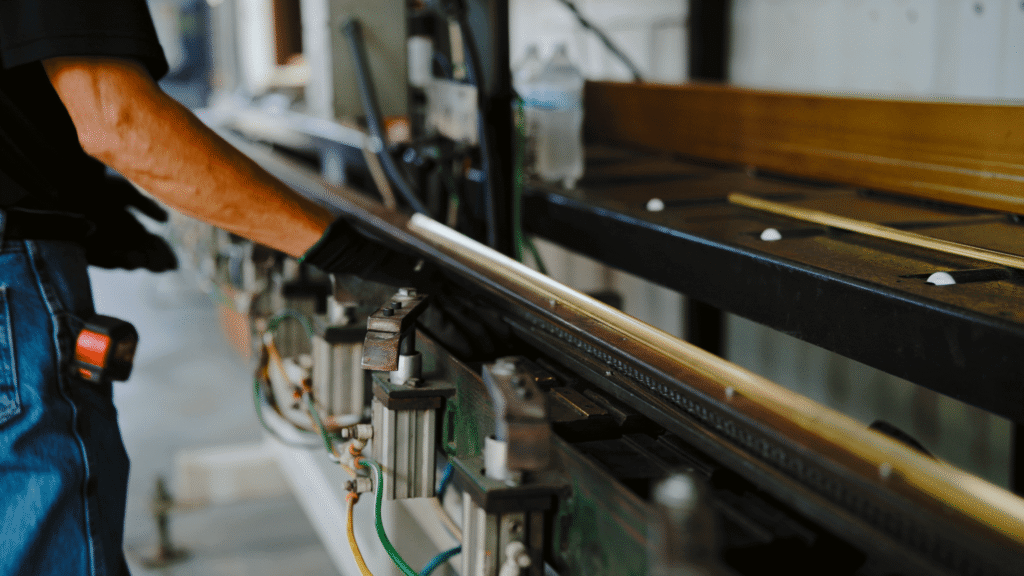 Technician guiding a solid bronze extrusion through a precision machine using bronze window frame production