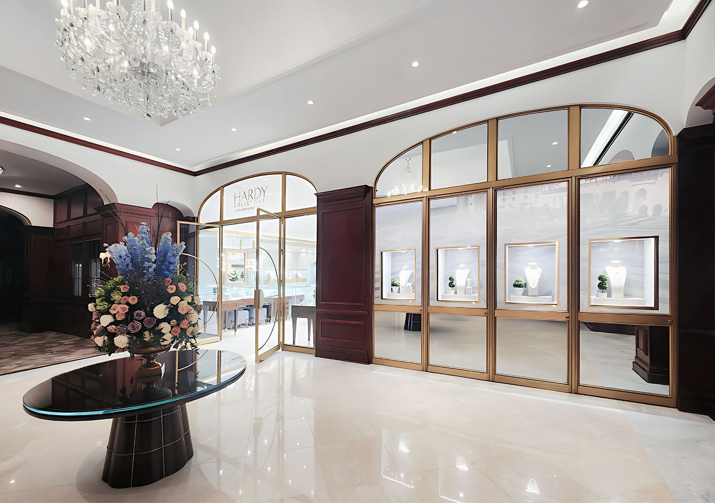Entrance to Hardy Collective luxury jewellery store featuring gold-rimmed round doors and windows, four elegant glass display windows, and a black glass table with a vibrant floral arrangement in shades of blue, pink, and purple